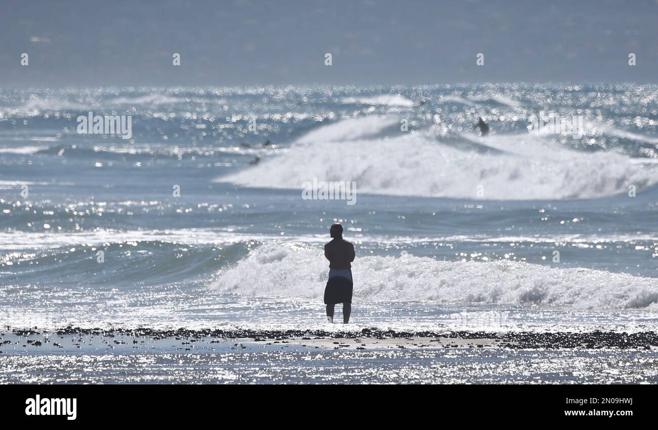 A beach goer watches surfers at a beach in Encinitas, Calif., Tuesday ...