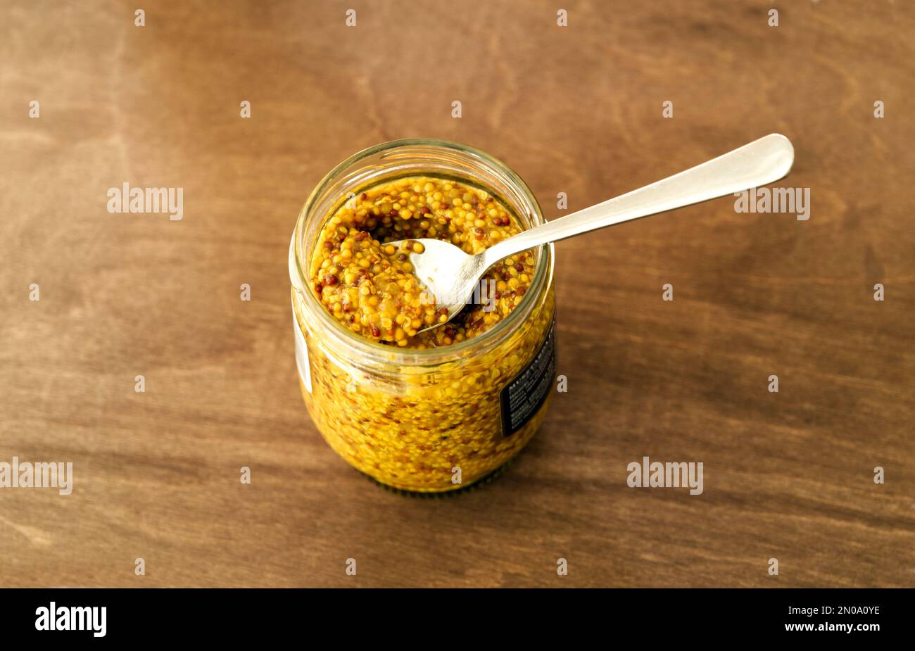 Open jar of french wholegrain yellow mustard with a spoon inside top