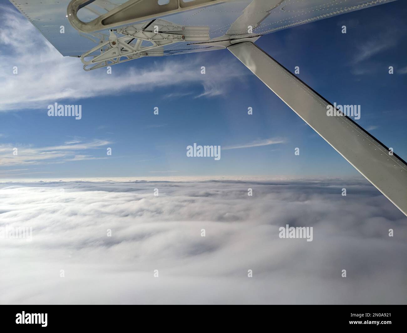 Window view from light general aviation aircraft. Strut and wing of semi-cantilever high-wing airplane flying over the clouds on a sunny day. Stock Photo
