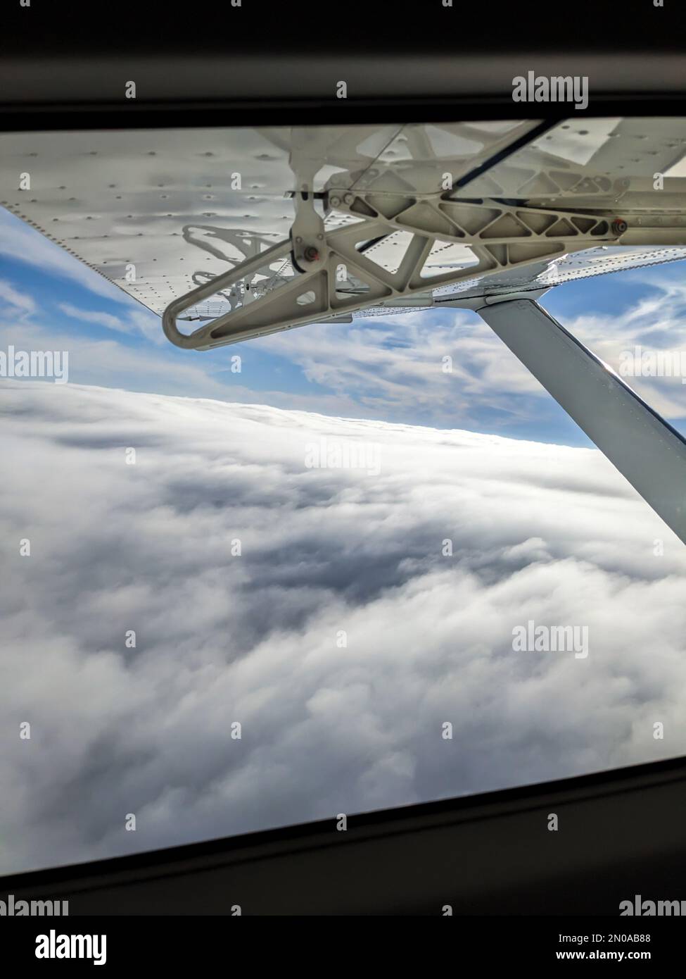 Window view from light general aviation aircraft. Strut and wing of semi-cantilever high-wing airplane flying over the clouds on a sunny day. Stock Photo
