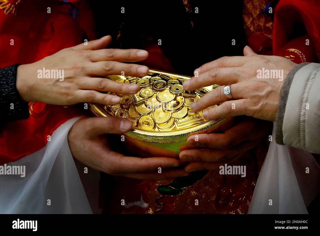 A man and a woman touch gold coins which are carried by a worker dressed as  a God of Fortune at a shopping mall in Beijing, Friday, Feb. 12, 2016.  Millions of