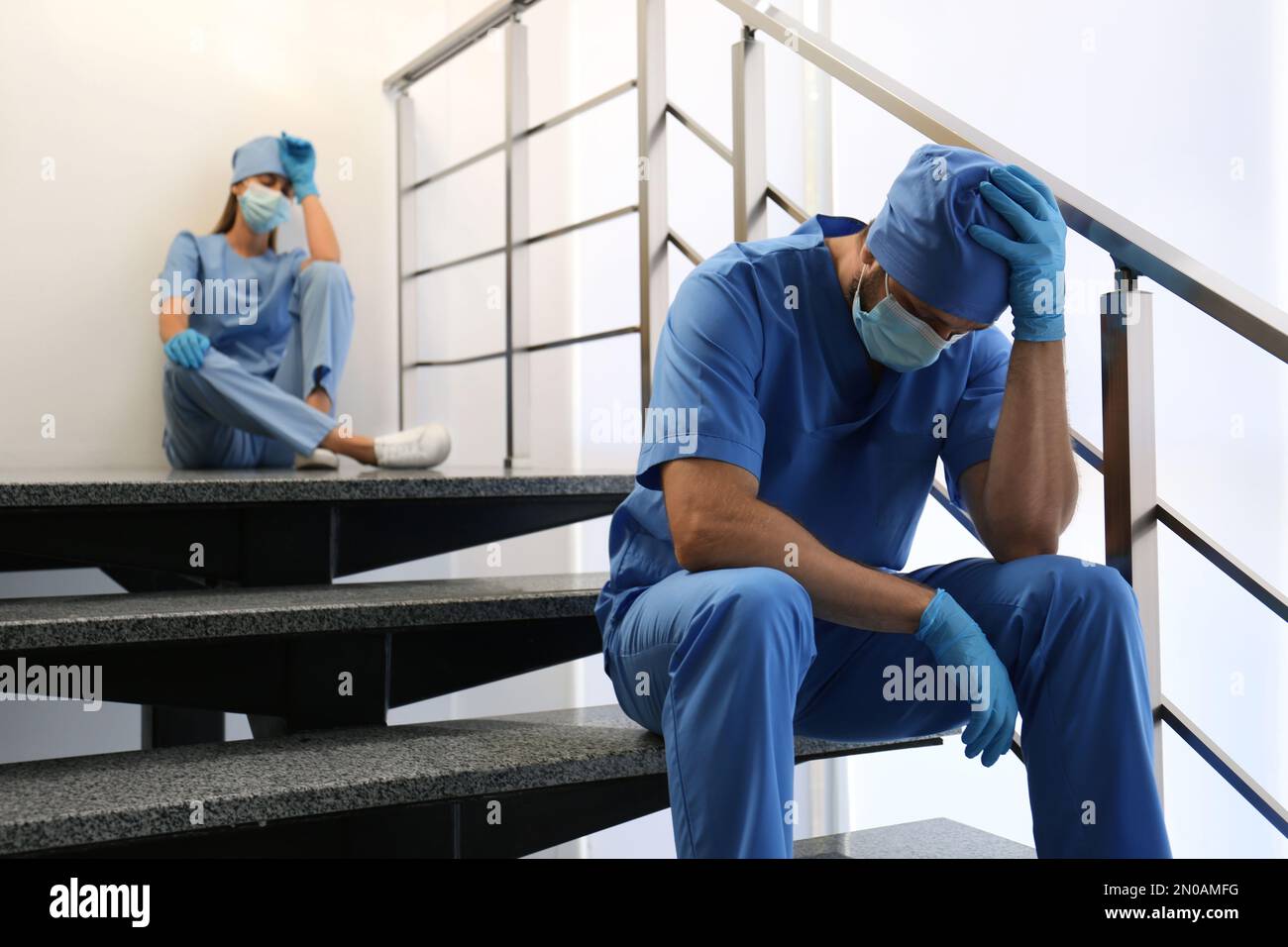 Exhausted doctors sitting on stairs indoors. Stress of health care