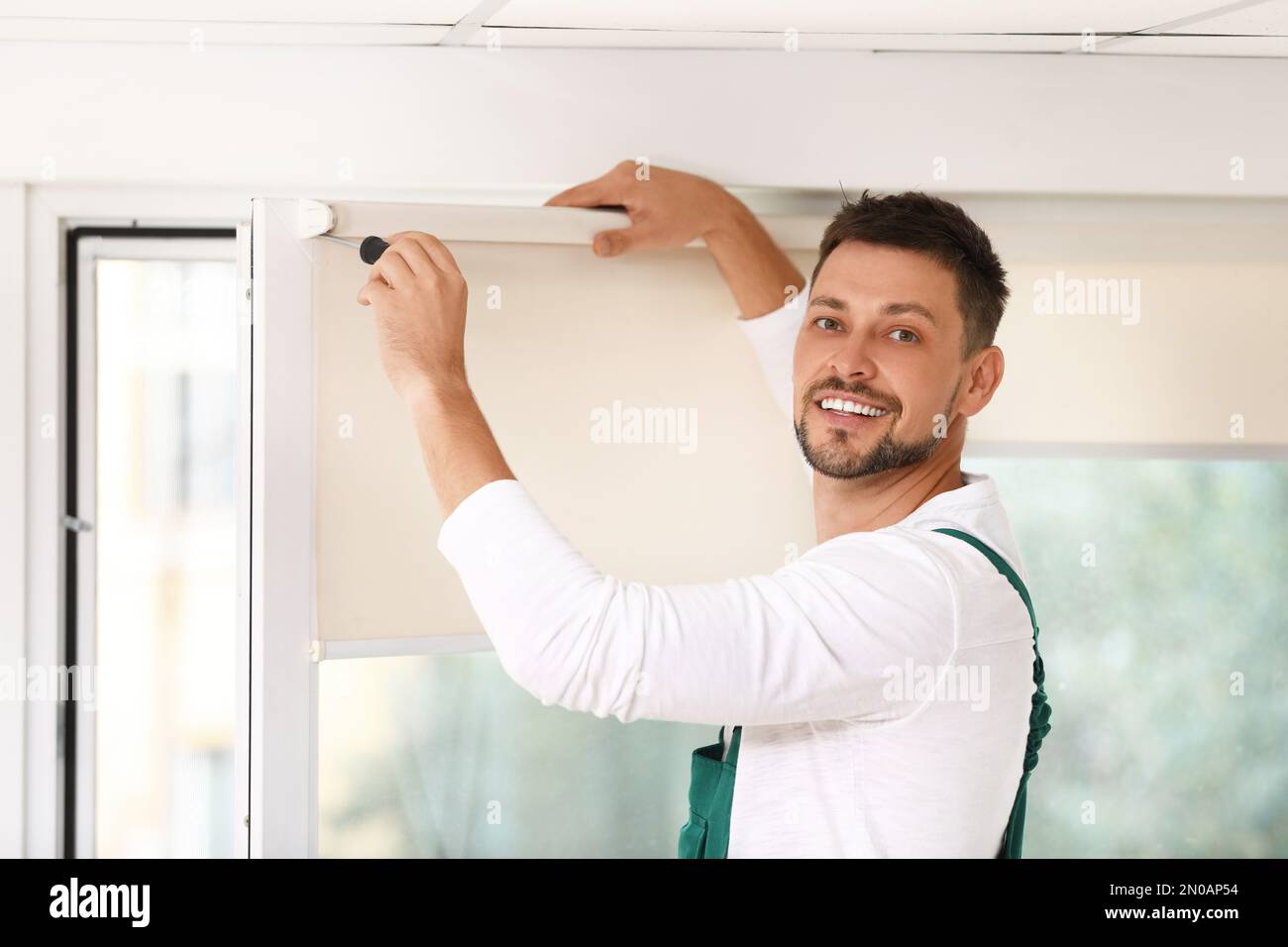 Handyman with screwdriver installing roller window blind indoors Stock Photo