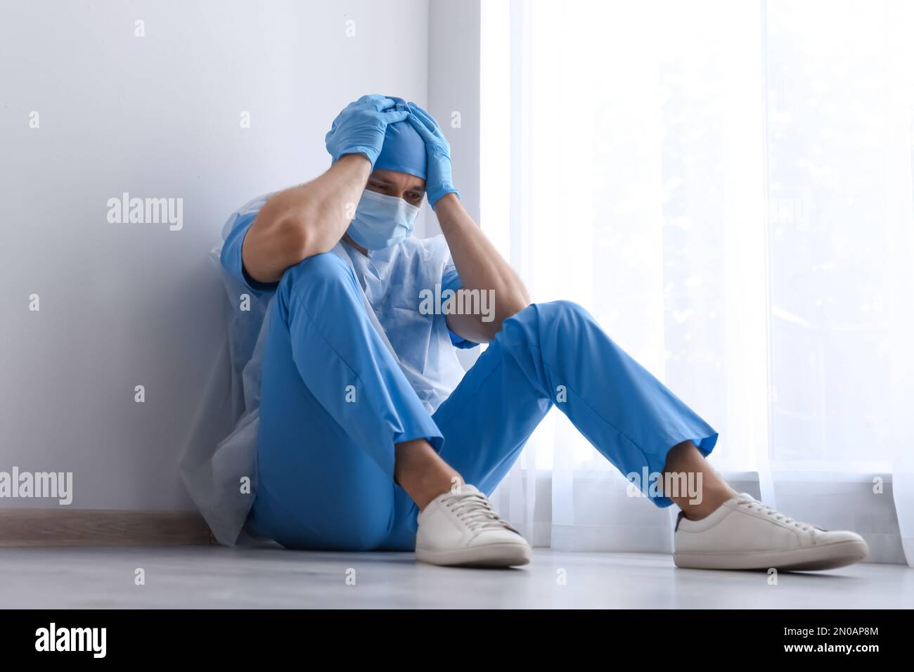 Exhausted doctor sitting on floor indoors. Stress of health care