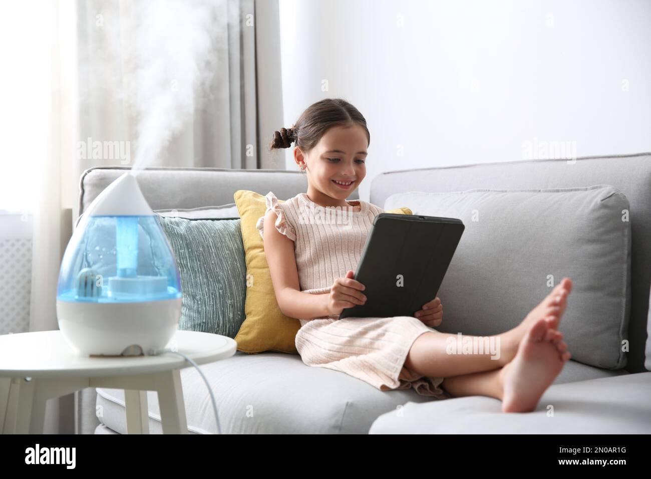 Little girl using tablet in room with modern air humidifier Stock Photo ...