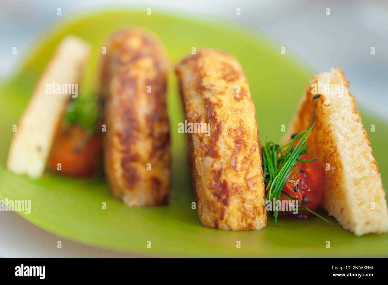 Close-up of Spanish Omelette with two slices of toast, cherry tomatoes, and chives. Breakfast meal of fried potatoes and eggs on a neon green plate. Stock Photo