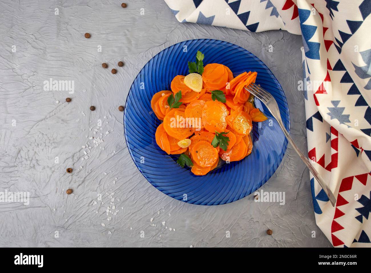 Sautéed carrots with garlic and parsley on a blue glass plate, on cement table top, with fabric napkin, flat lay Stock Photo