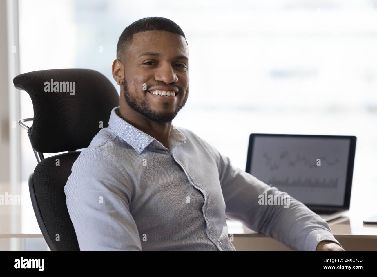 Cheerful confident young Black businessman sitting at office work table Stock Photo