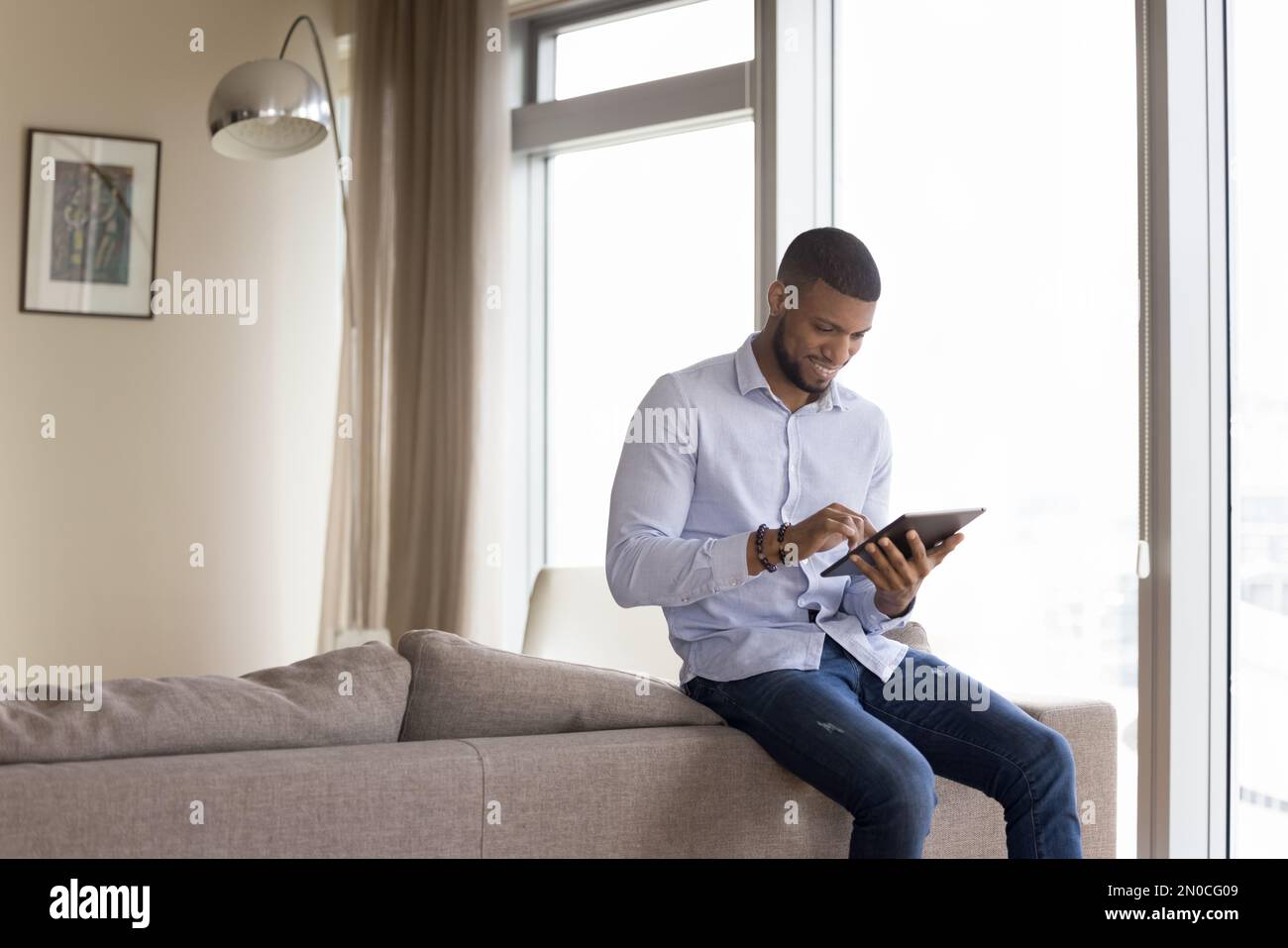 Happy handsome millennial African man touching tablet screen Stock Photo