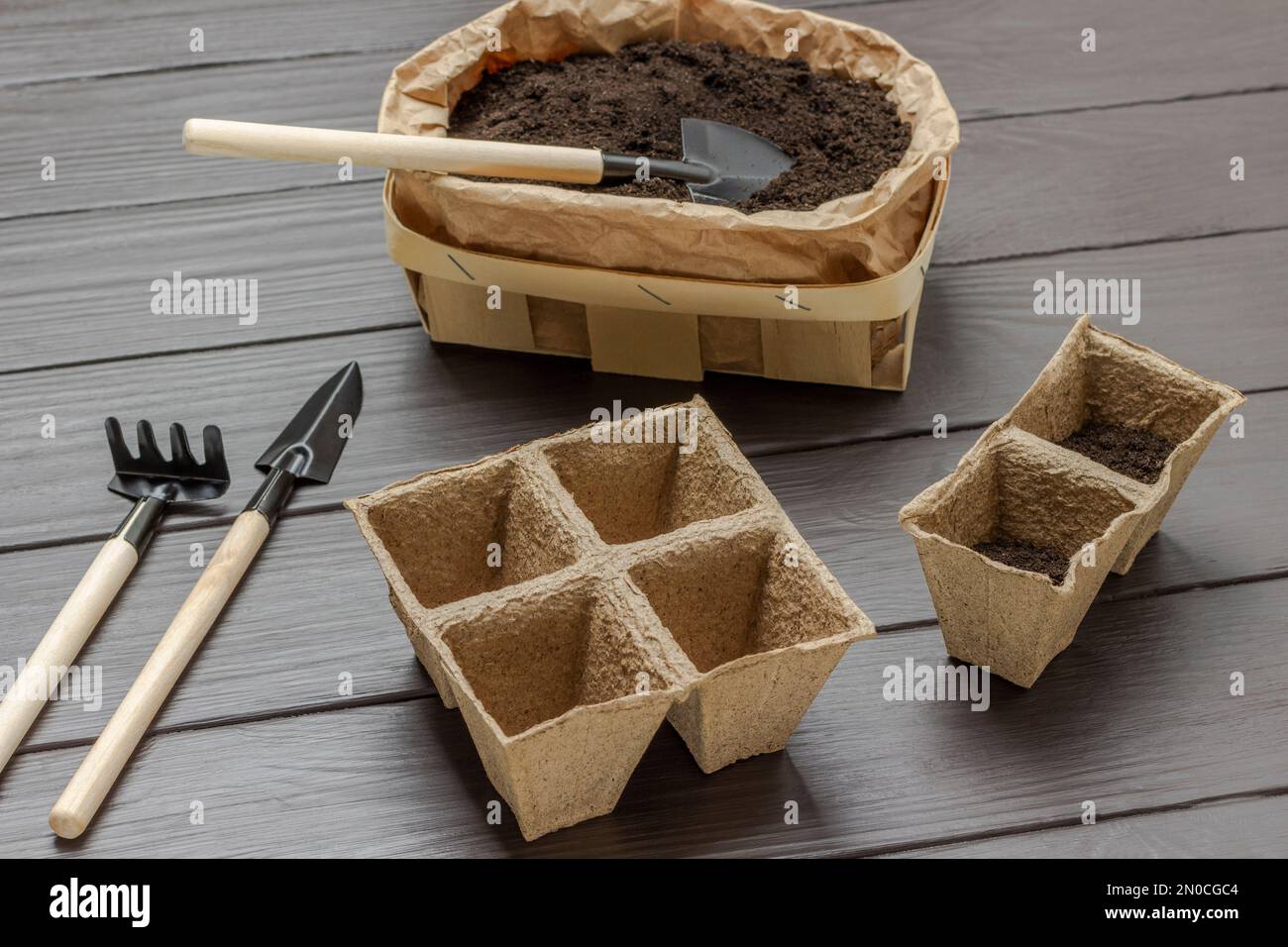 Garden shovel in a paper bag with soil. Rake, shovel and peat pots. Top view. Dark wooden
