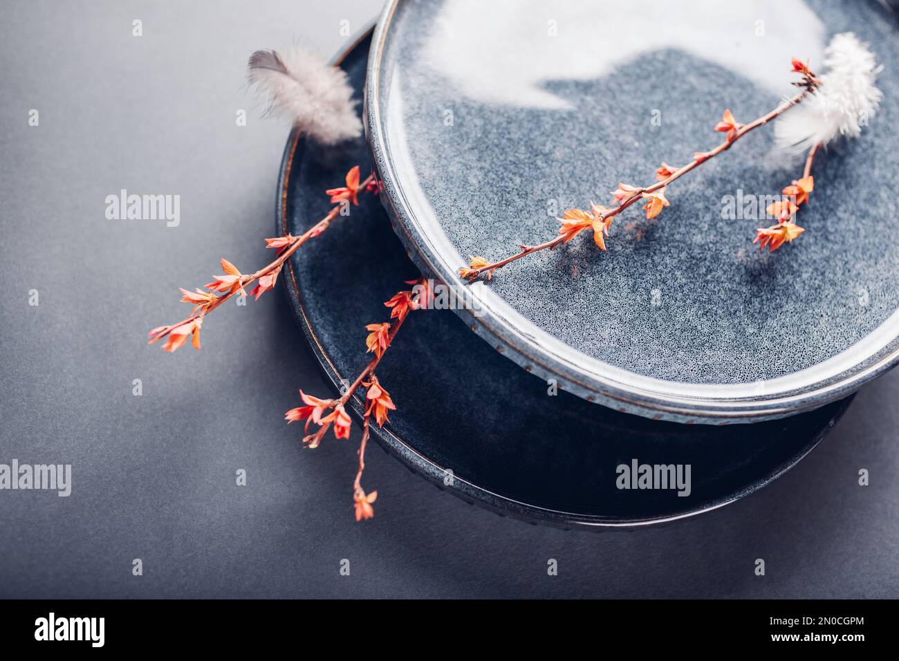Set of handmade round ceramic plates decorated with spring branches and feathers. Close up of lacquered blue vintage dishes on grey background. Stylis Stock Photo
