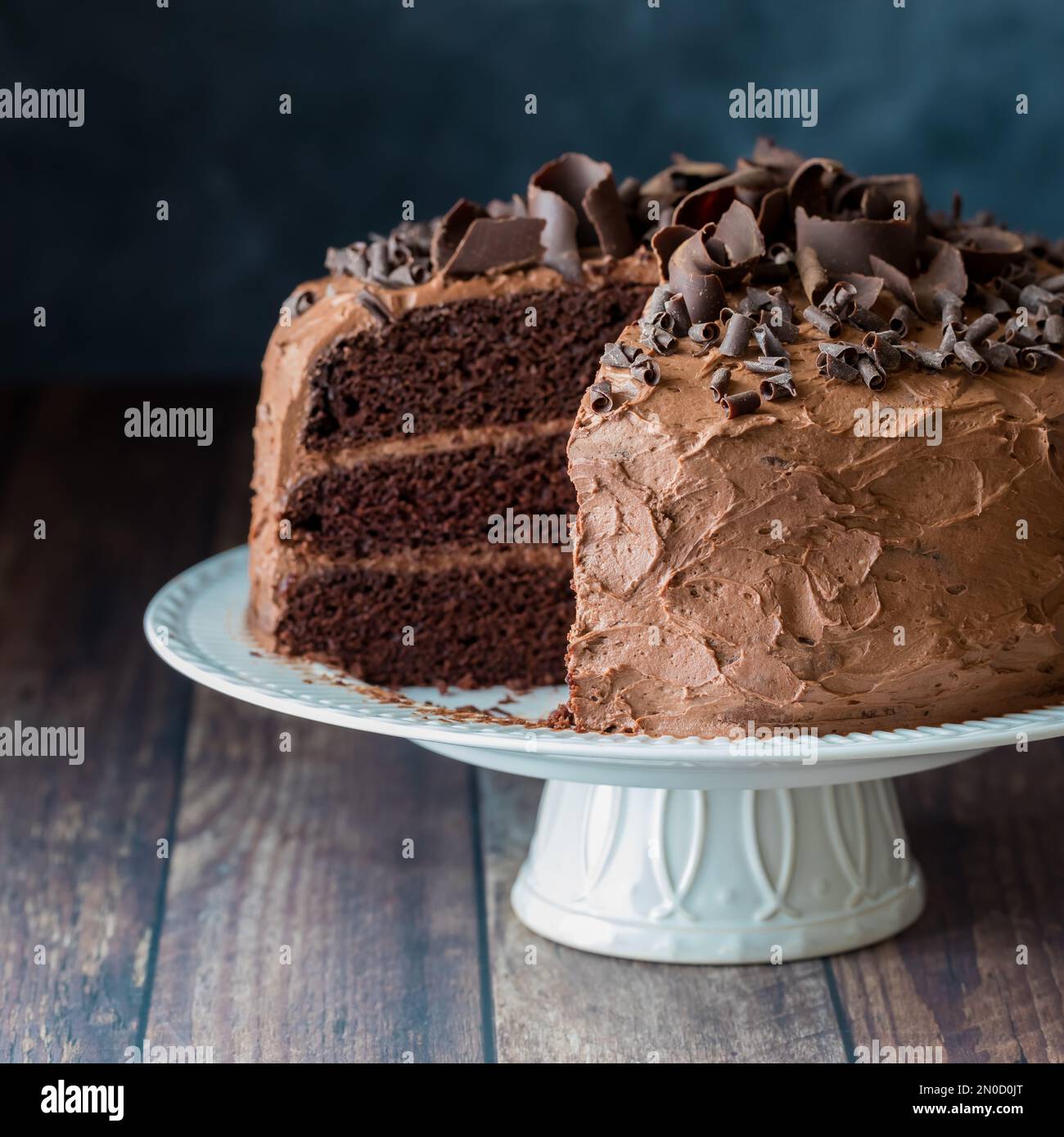 A triple layered moist chocolate cake with frosting and chocolate curls. Stock Photo