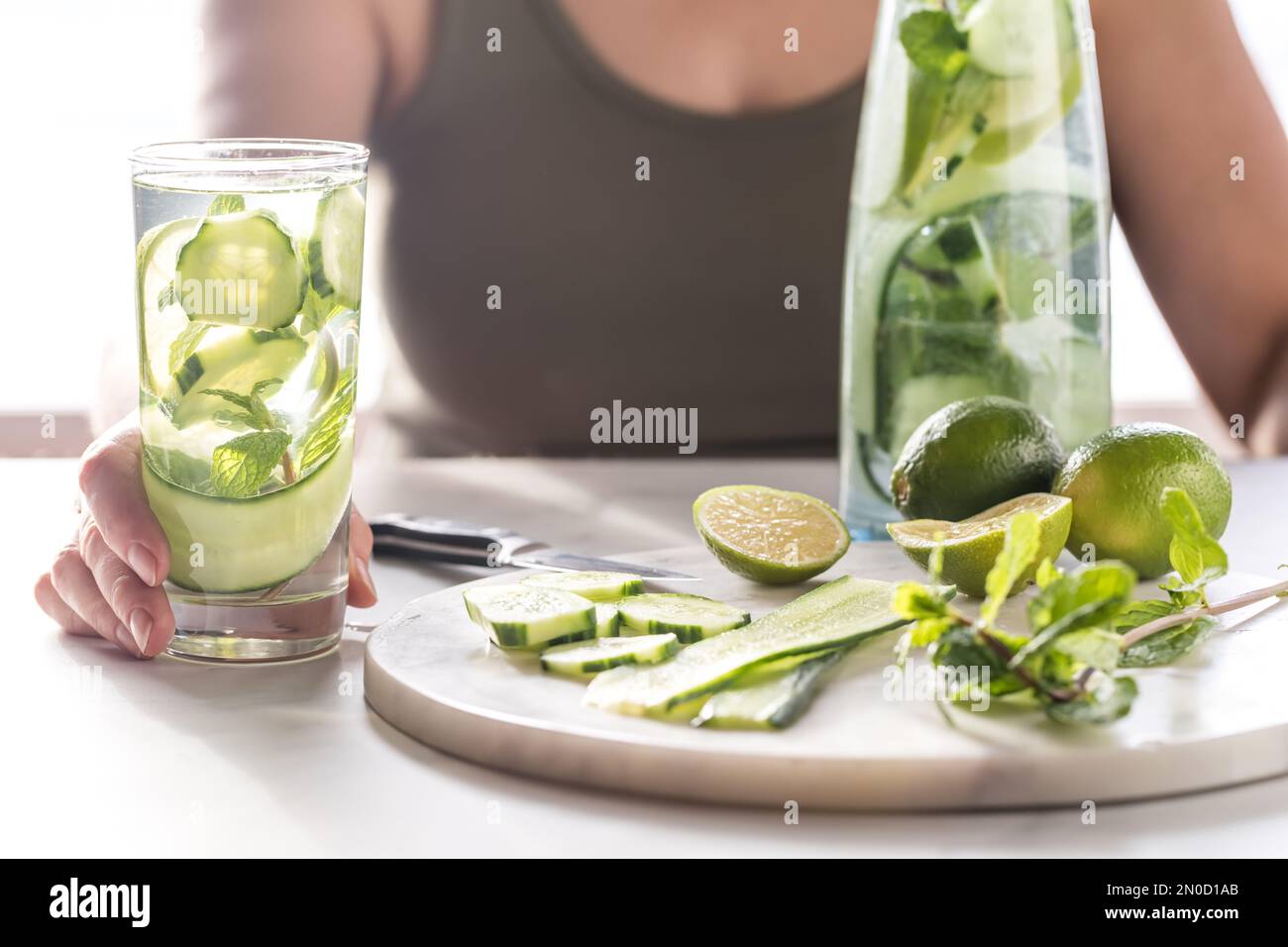 Woman holding a tall glass of infused cucumber water with lime and mint mixed in Stock Photo