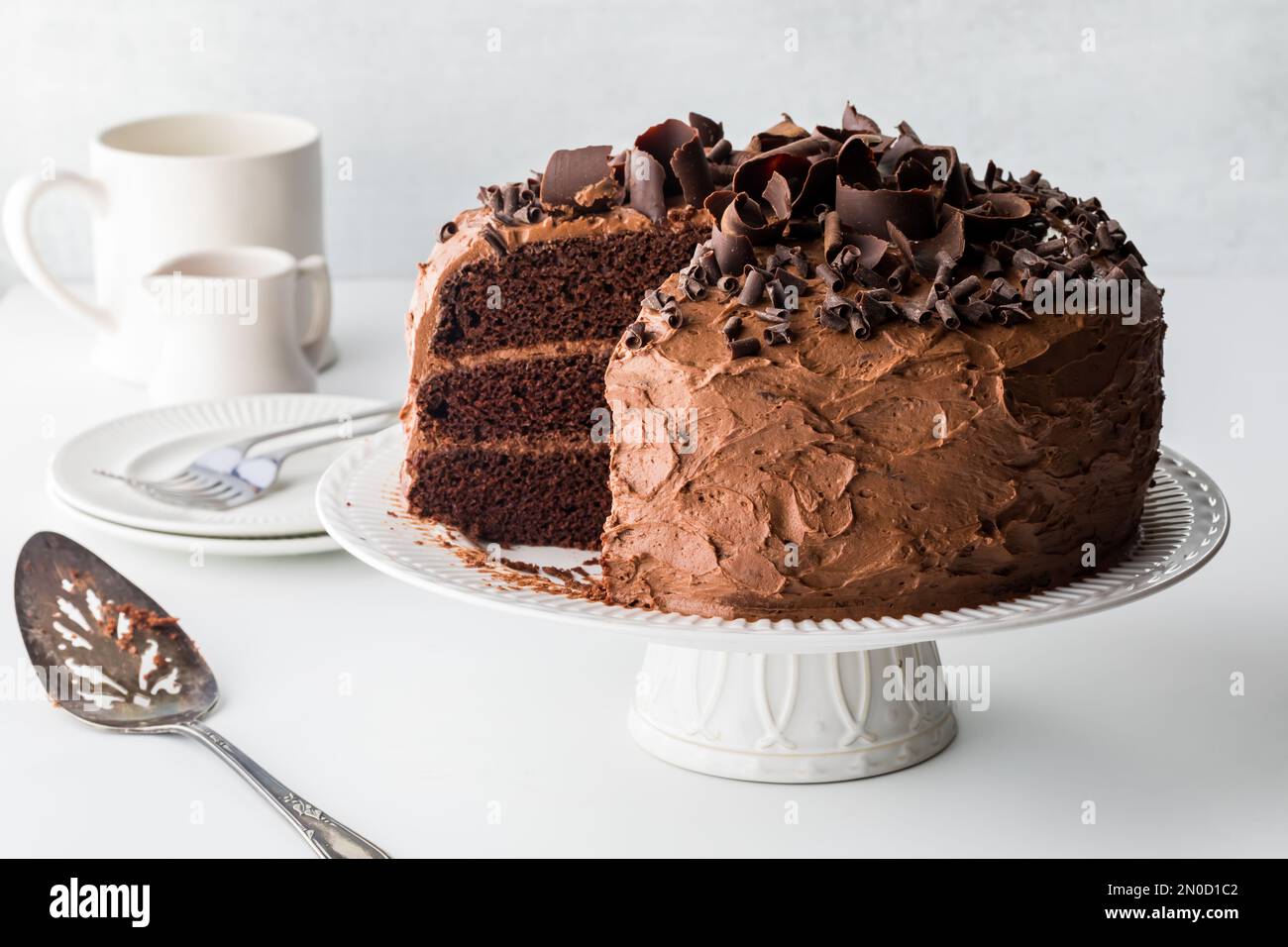 A triple layered chocolate cake with slices removed, against a light background. Stock Photo