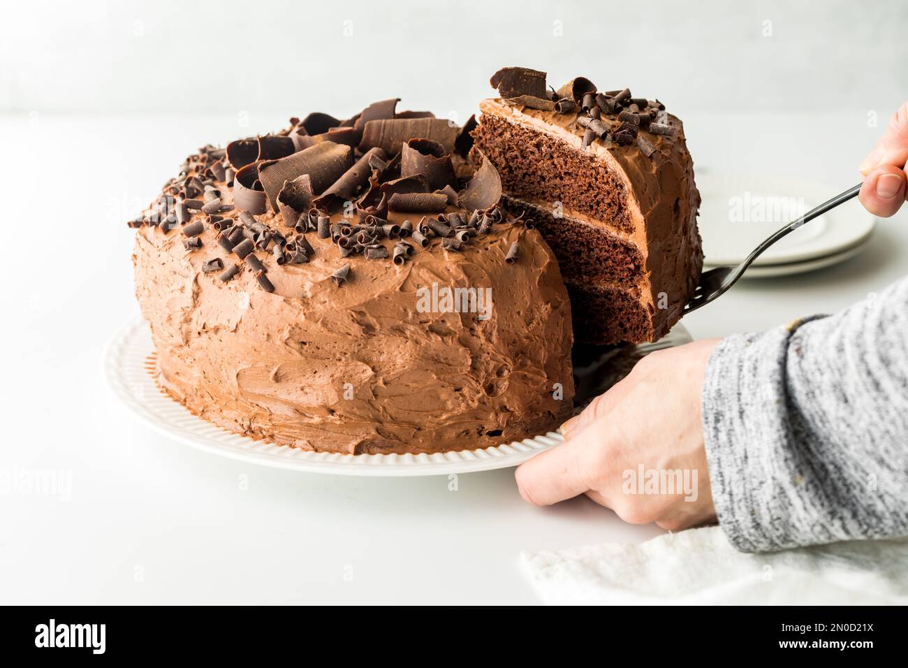 Hands removing a slice from a triple layered homemade chocolate cake. Stock Photo