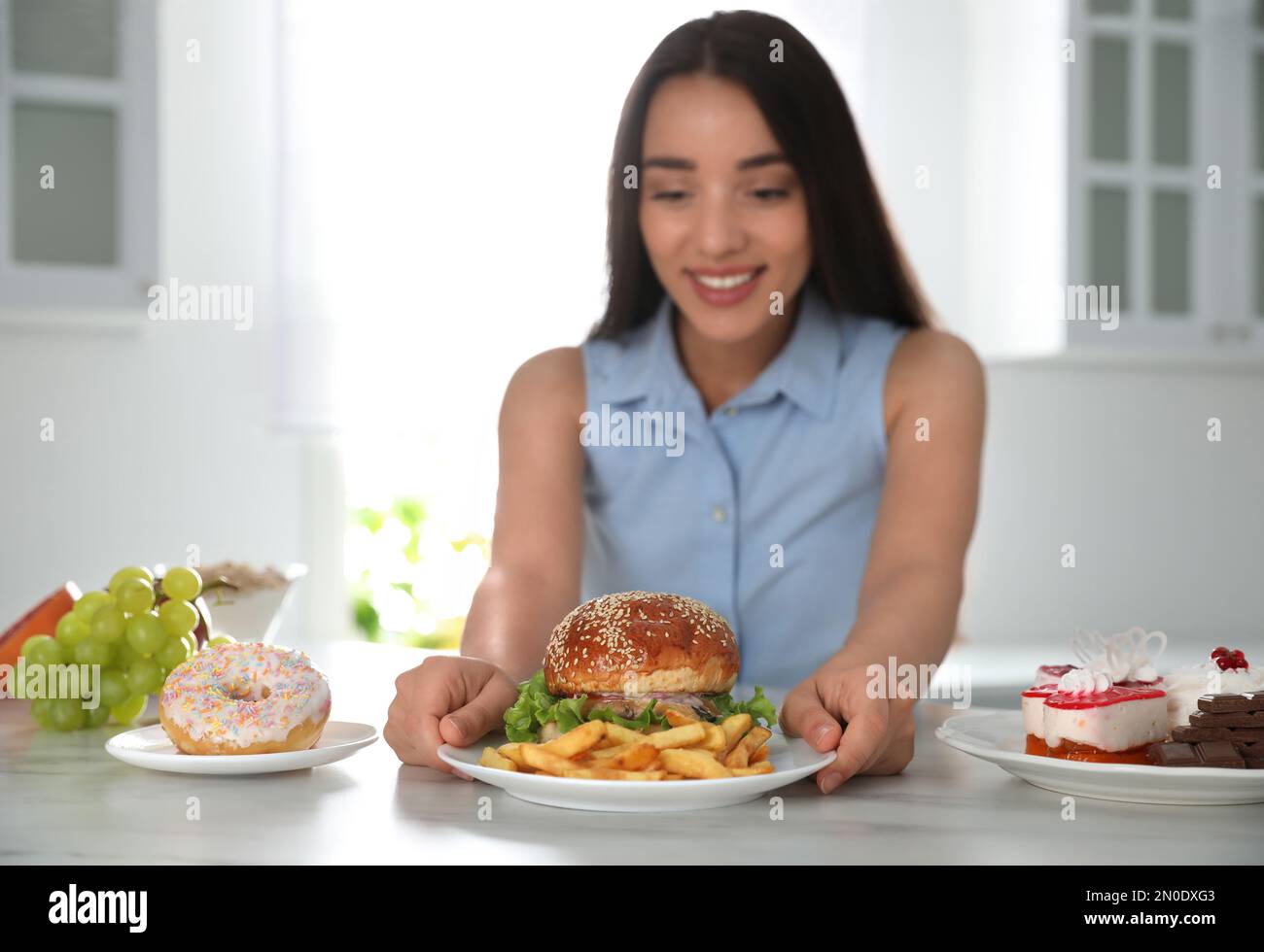 Concept of choice. Woman taking plate with tasty burger and French fries in kitchen, focus on food Stock Photo