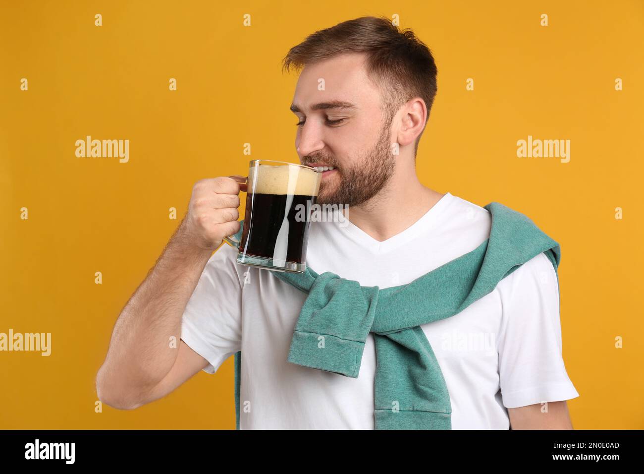Handsome man with cold kvass on yellow background. Traditional Russian summer drink Stock Photo