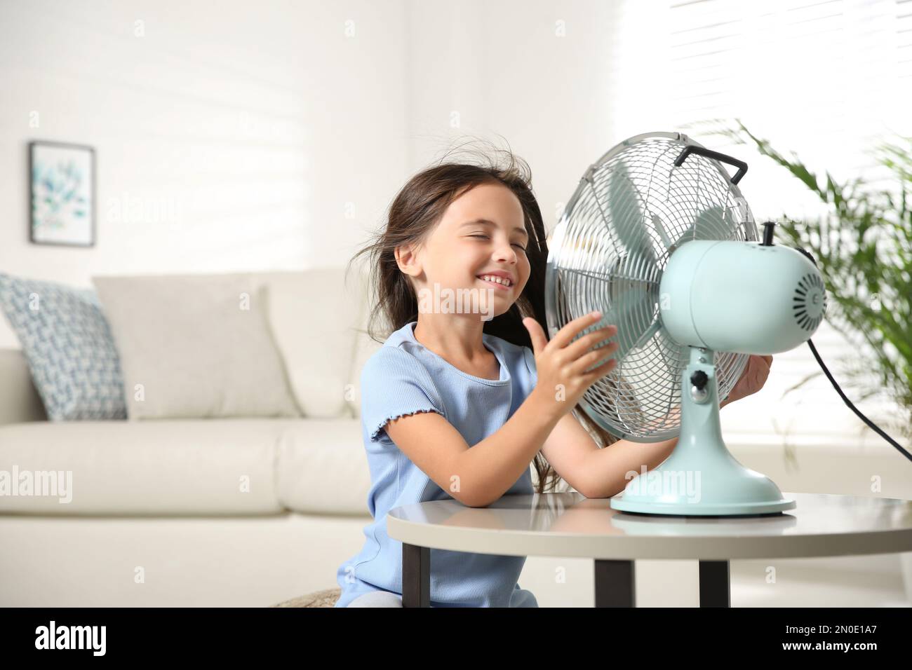 Little girl enjoying air flow from fan at home. Summer heat Stock Photo ...