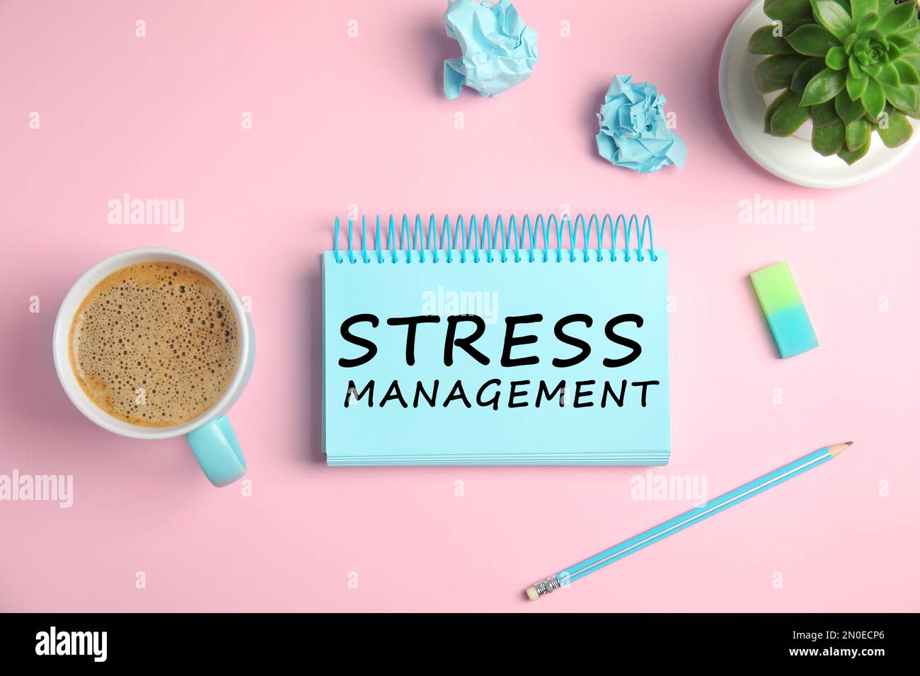Text Stress Management in notebook on pink background with stationery and cup of coffee, flat lay Stock Photo