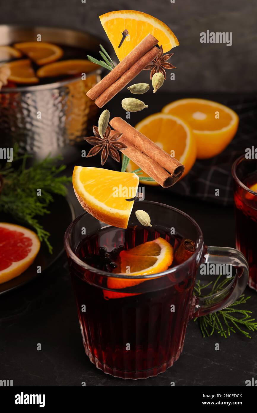 Cut orange and different spices falling into glass cup of mulled wine on table Stock Photo