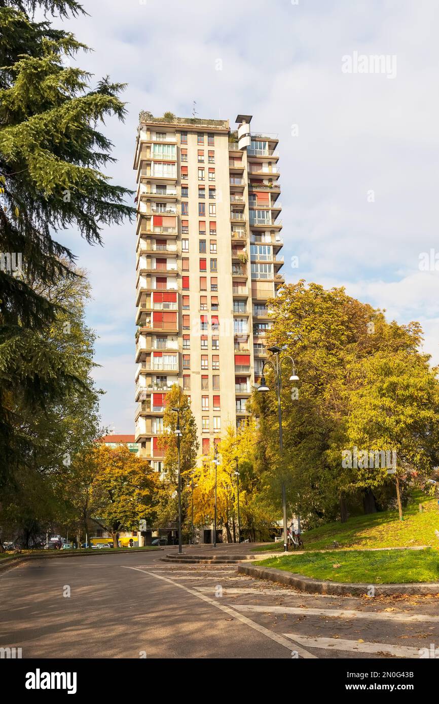 One multi-story residential building in the city among green trees against a light blue sky background Stock Photo