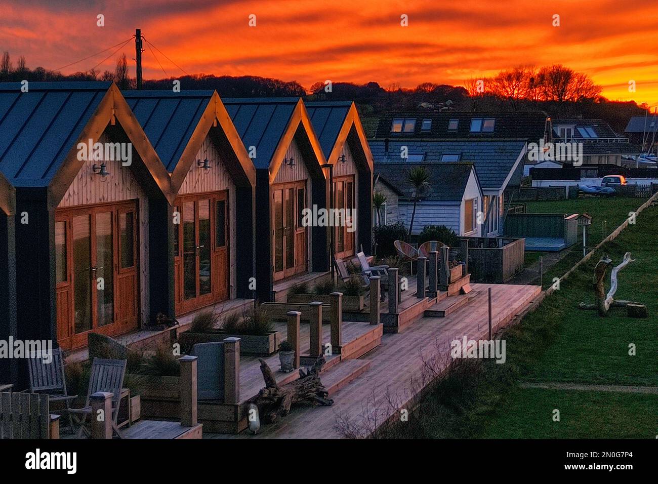 a row of same similar small tiny beachside living holiday homes on beach coast dramatic sunset reflecting building apex roof line Isle of Wight Stock Photo