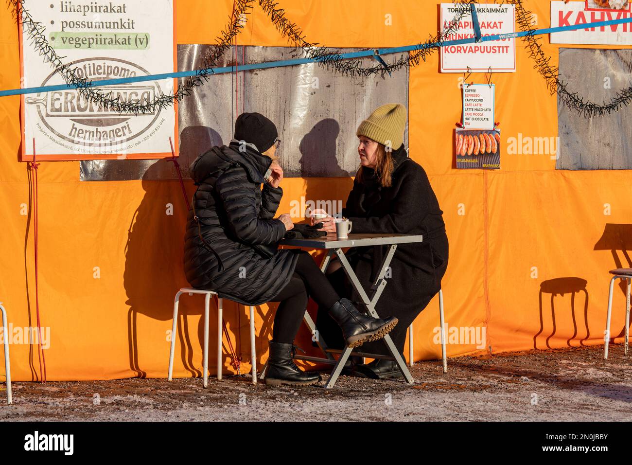 Women drinking coffee outside orange tent cafe on a sunny winter day at Kauppatori or Market Square in Helsinki, Finland Stock Photo