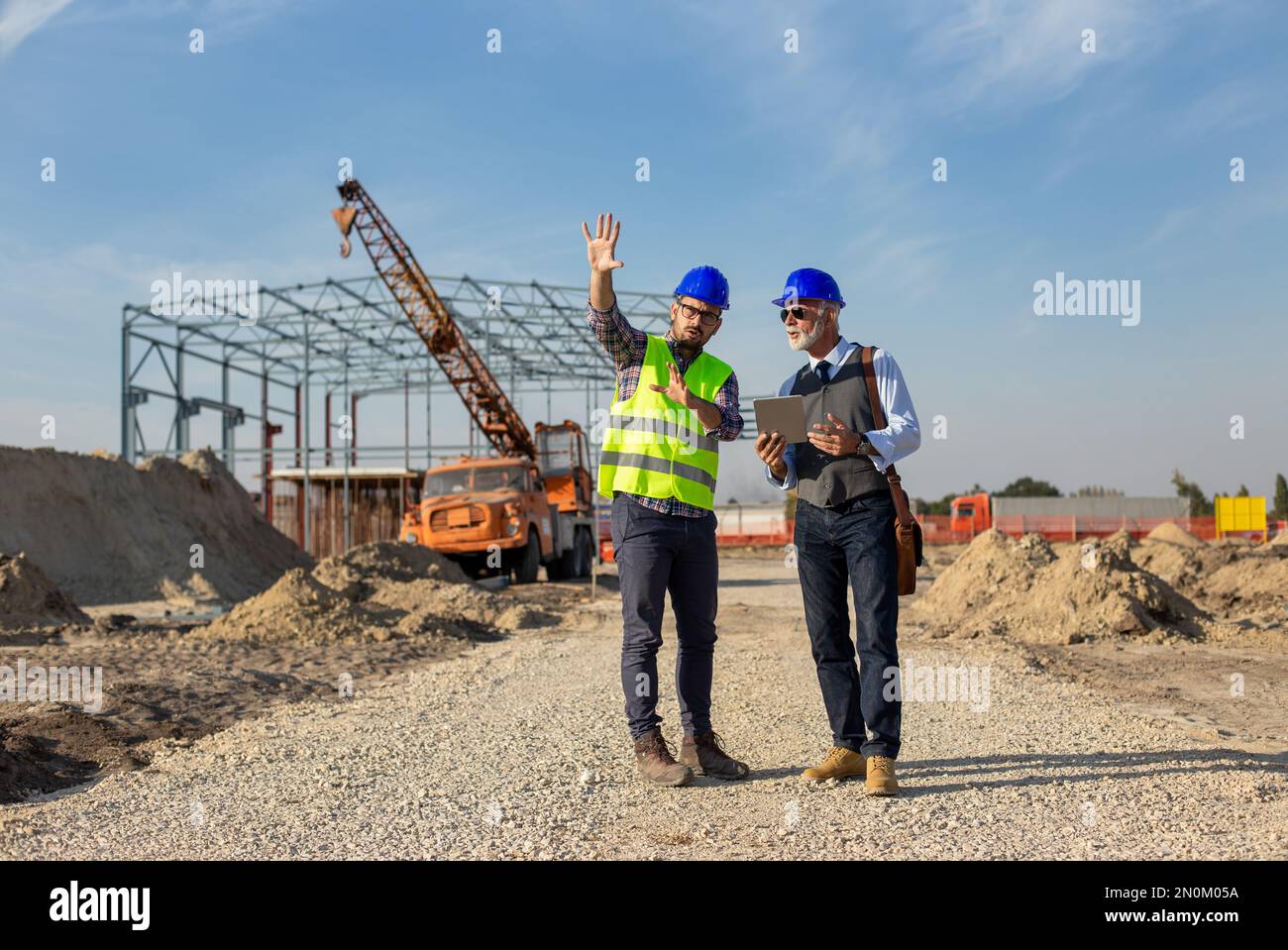 Two satisfied engineers talking at building site with construction structure in background Stock Photo