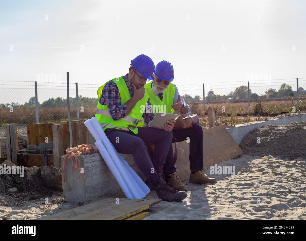 Two engineers with helmets and vests looking at tablet and talking about project at building site Stock Photo