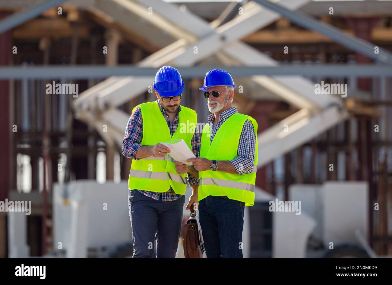 Two engineers with helmets and vests talking at building site in front of metal construction Stock Photo