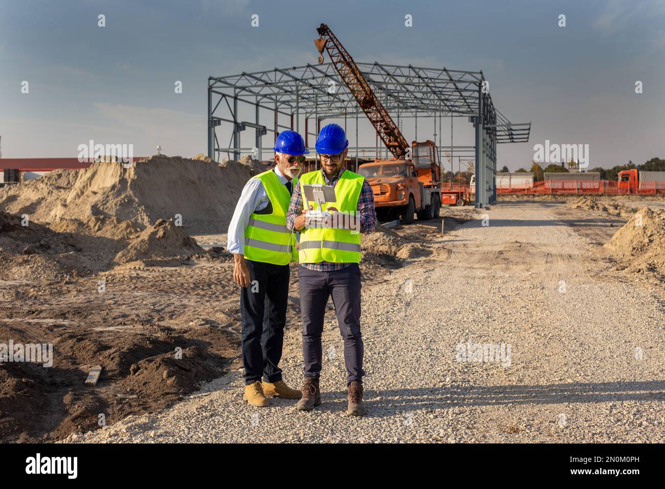 Two engineers with helmets and vests operating with drone by remote control. Technology innovations in construction industry Stock Photo