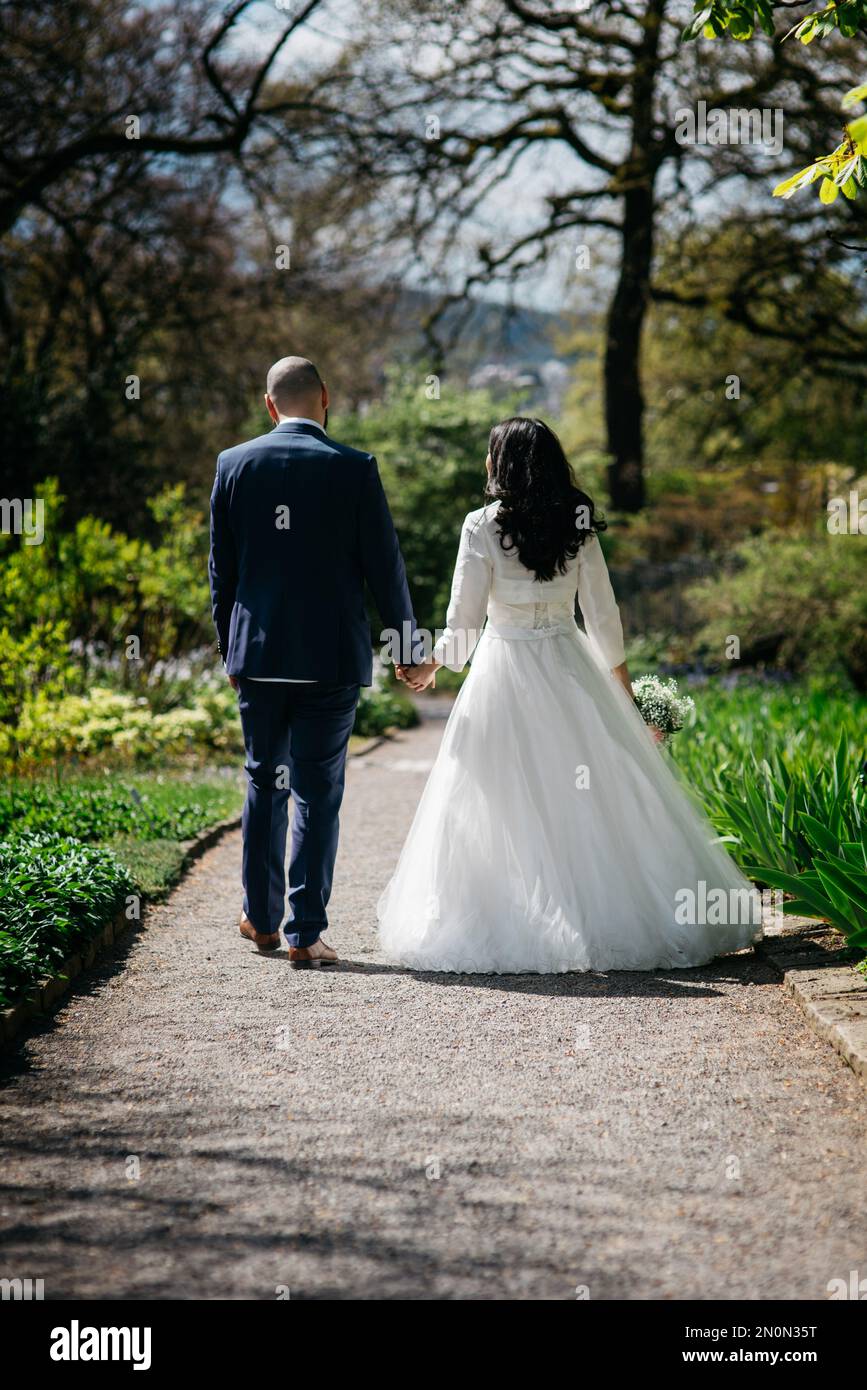 A vertical back view of the bride and the groom walking in a park Stock ...