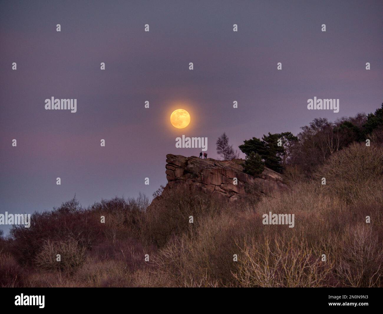 People watching the Full Snow Moon rise over the top of Black Rocks Derbyshire UK HDR Stock Photo