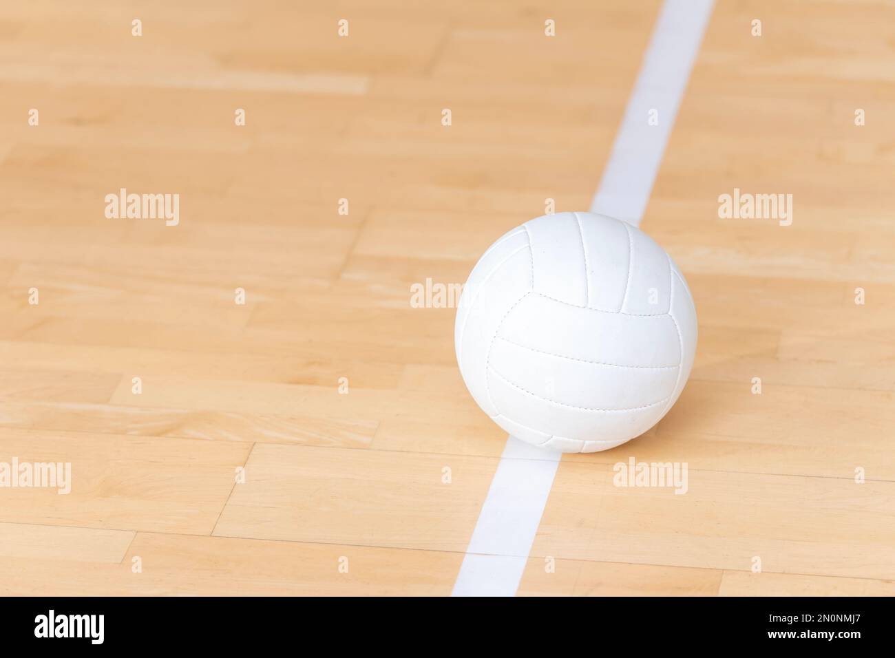 Volleyball ball on hardwood court floor with white line. Team sport