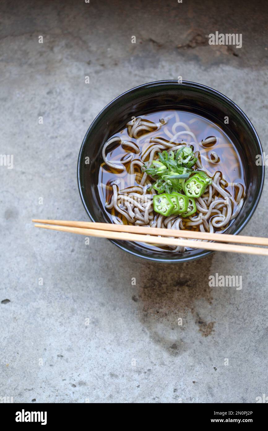 A black china bowl of noodles and broth with sliced chillis and an egg. Stock Photo