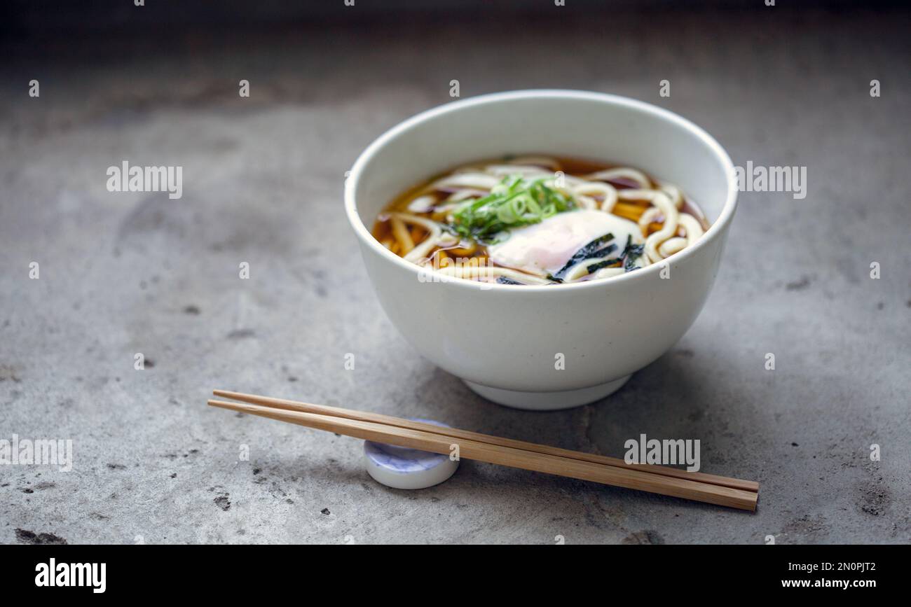 A bowl of noodles, vegetables and broth and a set of chopsticks. Stock Photo