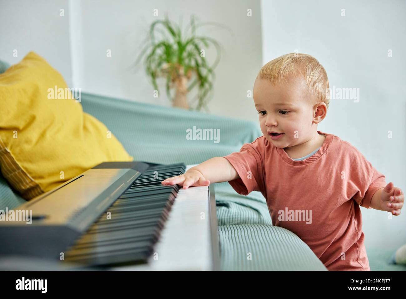 Toddler playing with electronic piano keyboard on sofa Stock Photo