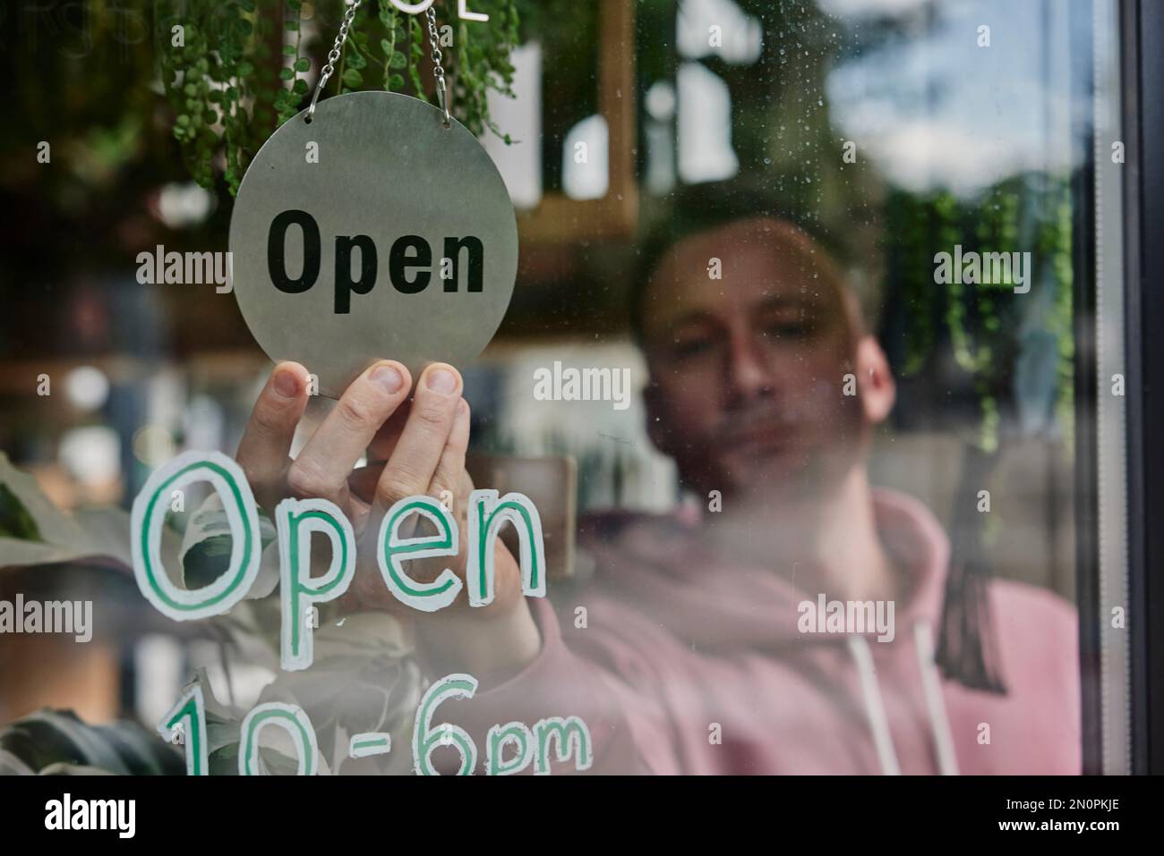 Man placing Open sign in window of shop Stock Photo