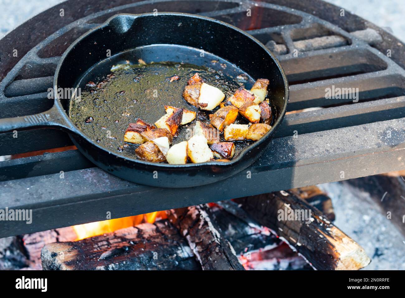 Cooking fried potato hashbrowns in a cast iron skillet over a campfire