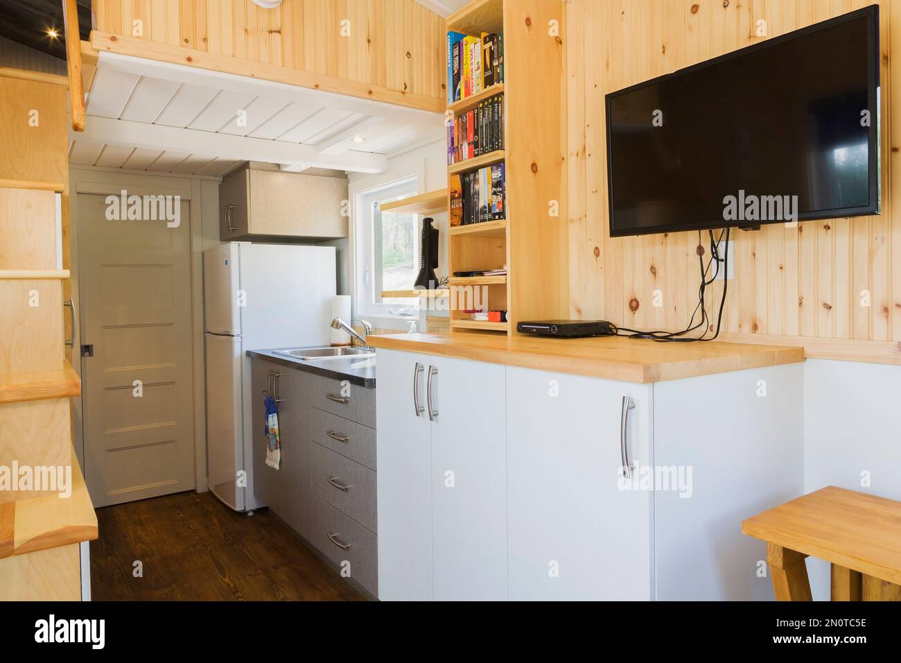Partial view of pinewood stairs leading to upper floor bedroom, kitchen area and bathroom door in background inside 8 x 24 foot mobile mini house. Stock Photo