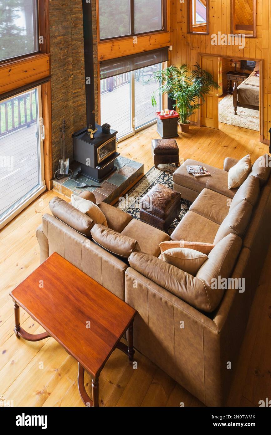 Top view of tan leather sectional sofa and wood burning stove in living room area of great room with cathedral ceiling inside milled log home. Stock Photo