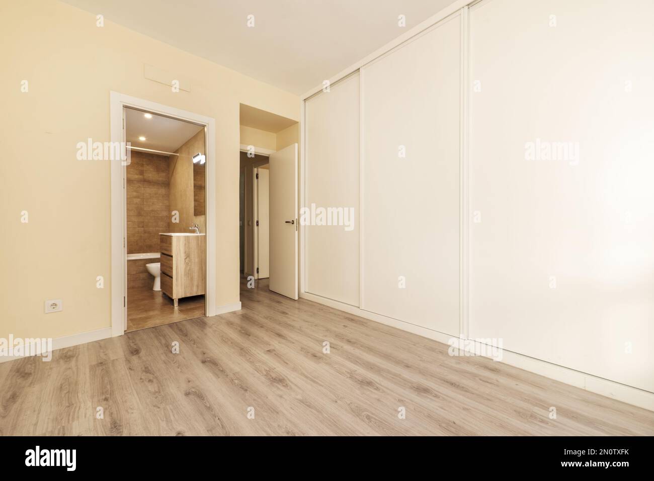 Empty bedroom with en-suite bathroom and a wall-to-wall white wooden sliding-door closet Stock Photo