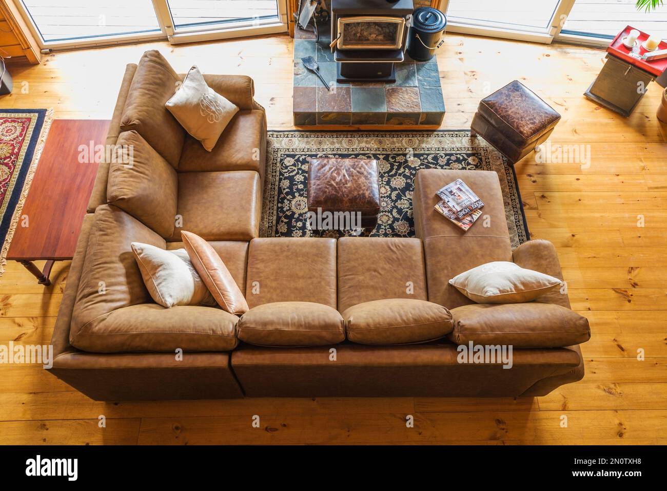 Top view of tan leather sectional sofa with wood burning stove on elevated natural stone base in living room area of great room in log cabin. Stock Photo