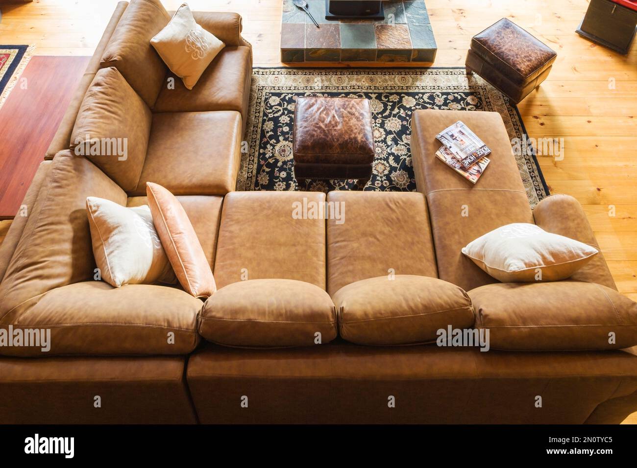 Top view of tan leather sectional sofa with wood burning stove on elevated natural stone base in living room area of great room in log cabin. Stock Photo