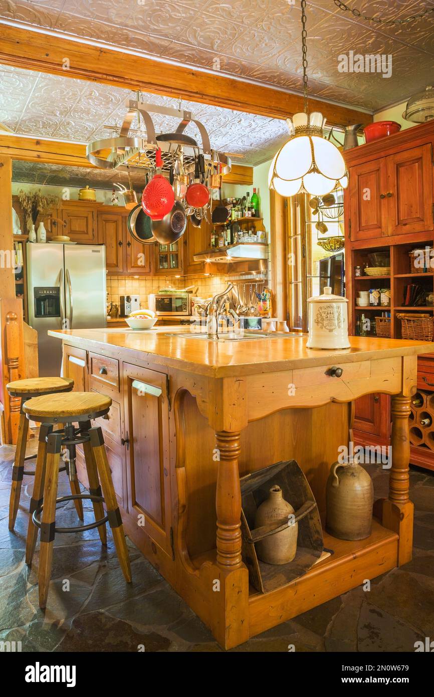 Kitchen with antique pine wood island, buffet, cabinets, slate floor and stamped vinyl panel on ceiling inside old circa 1850 home. Stock Photo