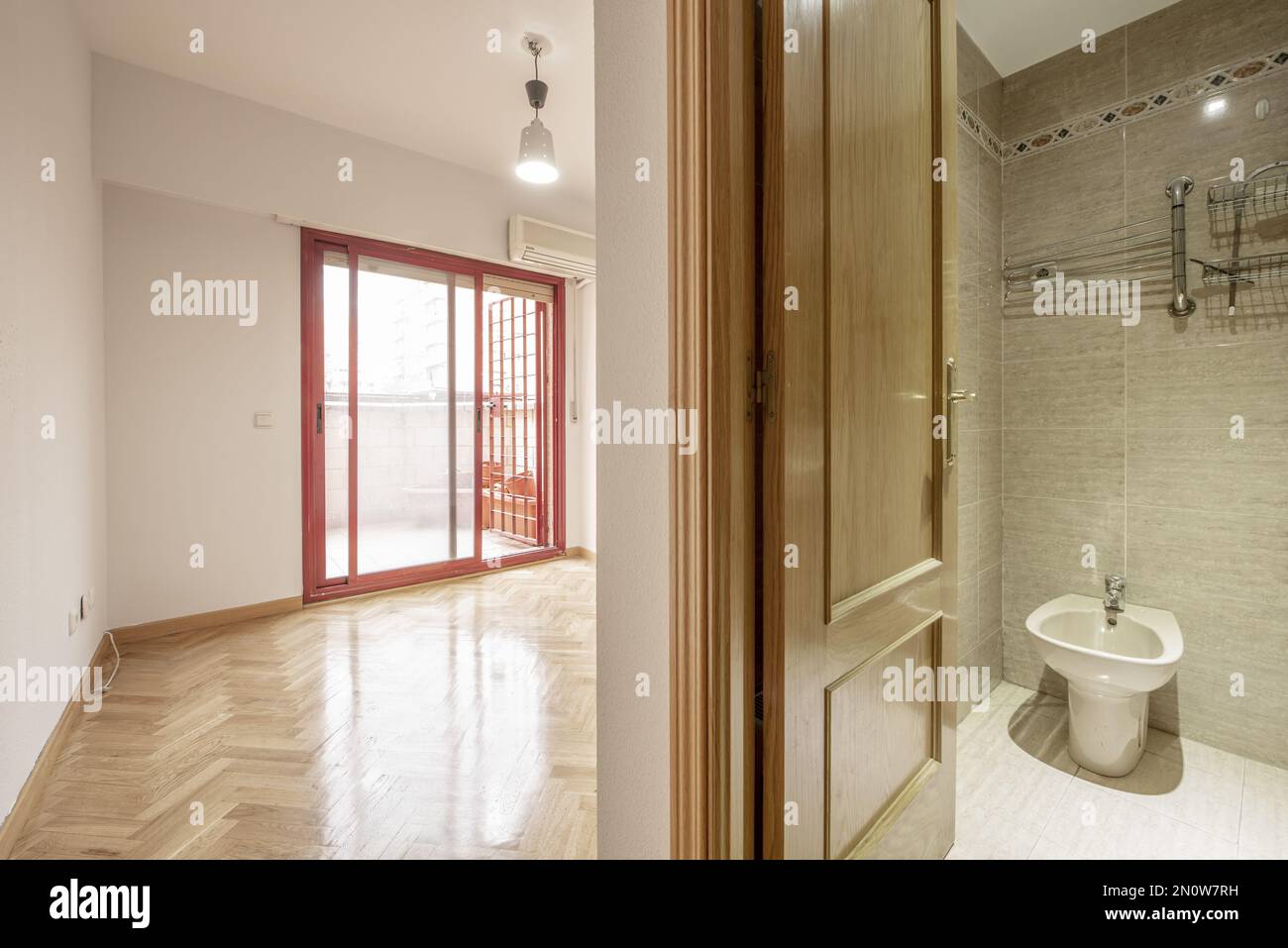 Bedroom with en-suite bathroom and exit to a terrace with red aluminum sliding doors with bars Stock Photo