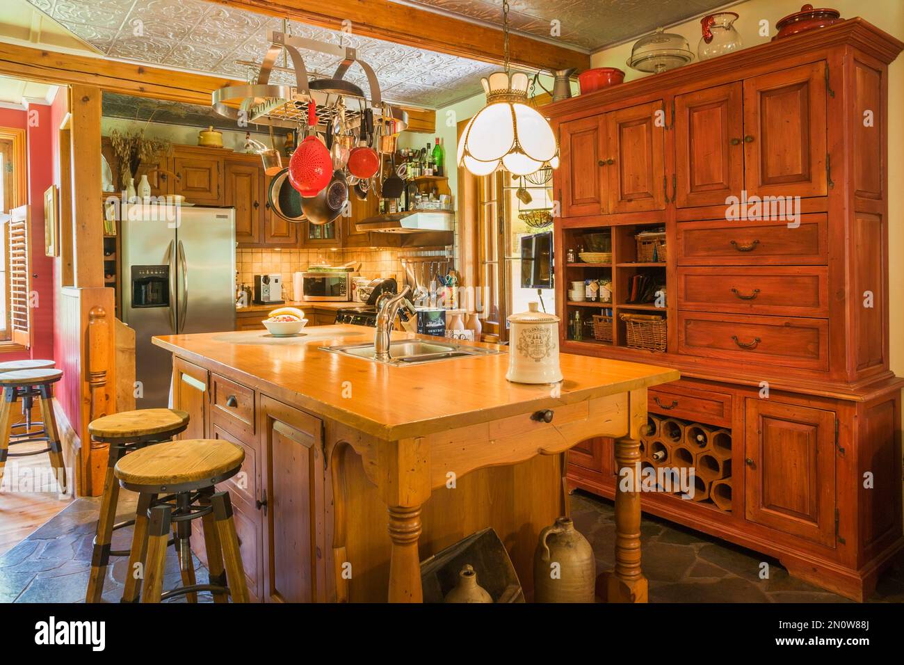 Kitchen with antique pine wood island, buffet, cabinets, slate floor and stamped vinyl panel on ceiling inside old circa 1850 home. Stock Photo