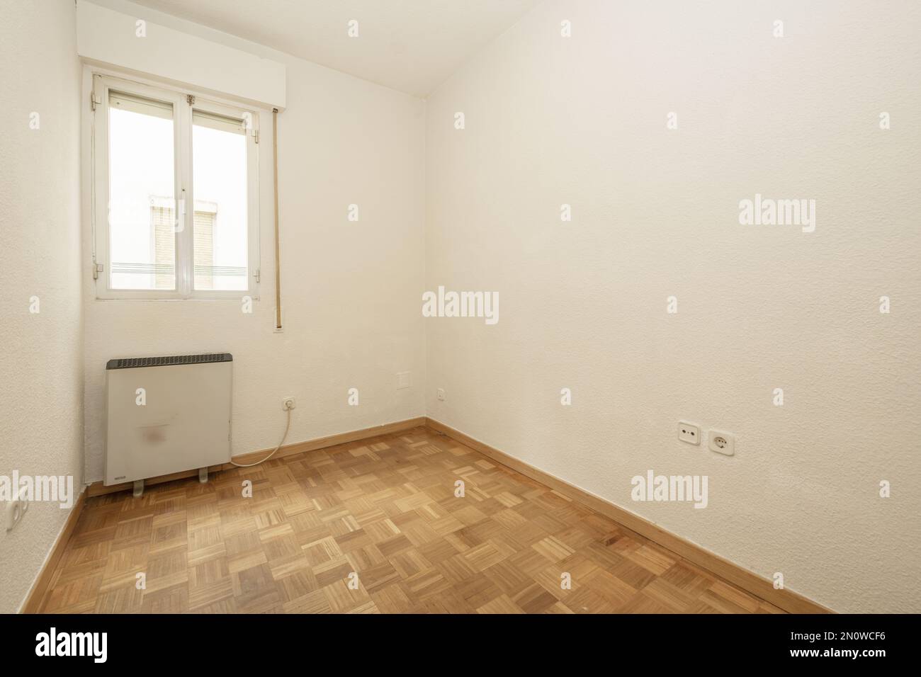 Empty room with gotelet white painted walls, white aluminum windows with electric heat accumulator below and oak parquet slatted floors laid in checke Stock Photo