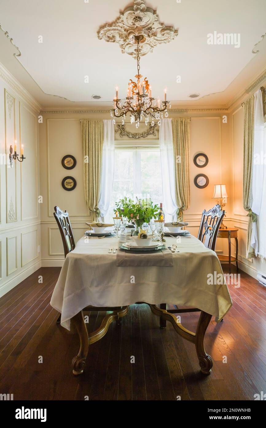 Set antique wooden dining table with 1850s dishes and hand sculptured high back chairs in dining room inside Renaissance period style home. Stock Photo