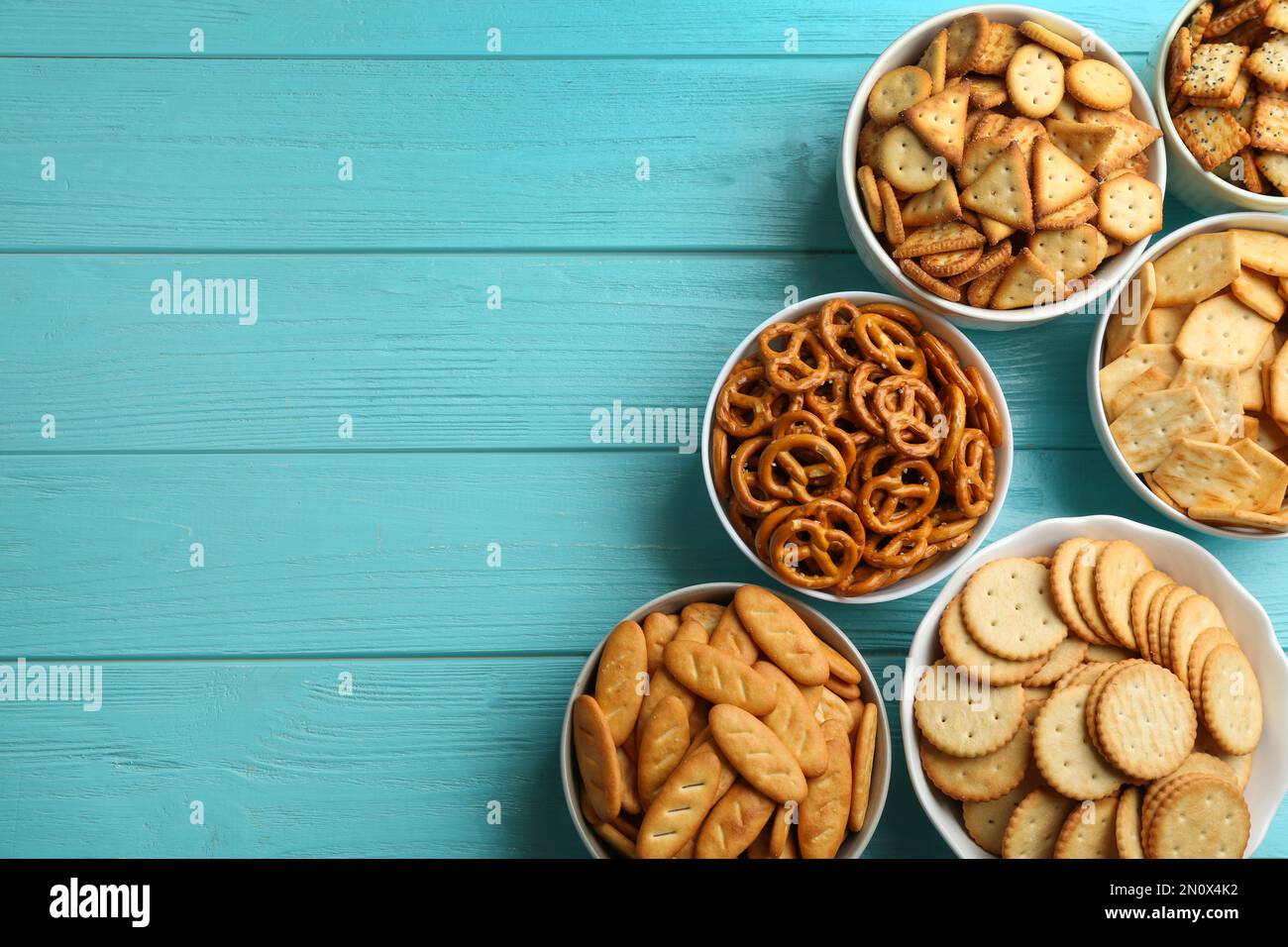 Different delicious crackers in bowls on turquoise wooden table, flat ...